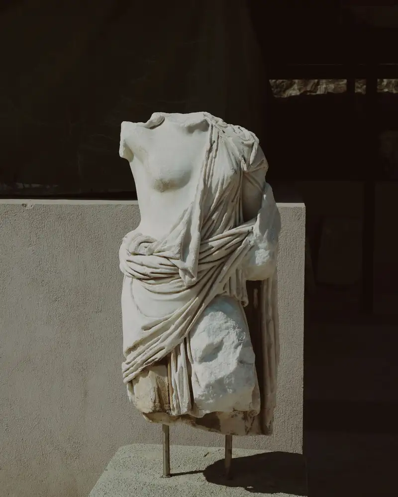 A draped classical marble torso on a stone plinth in daylight