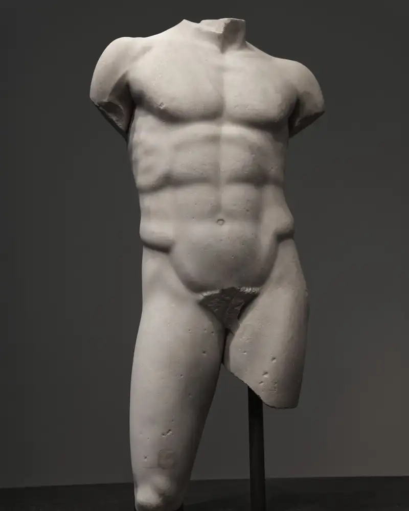 A white marble torso of a standing figure against a grey gallery wall