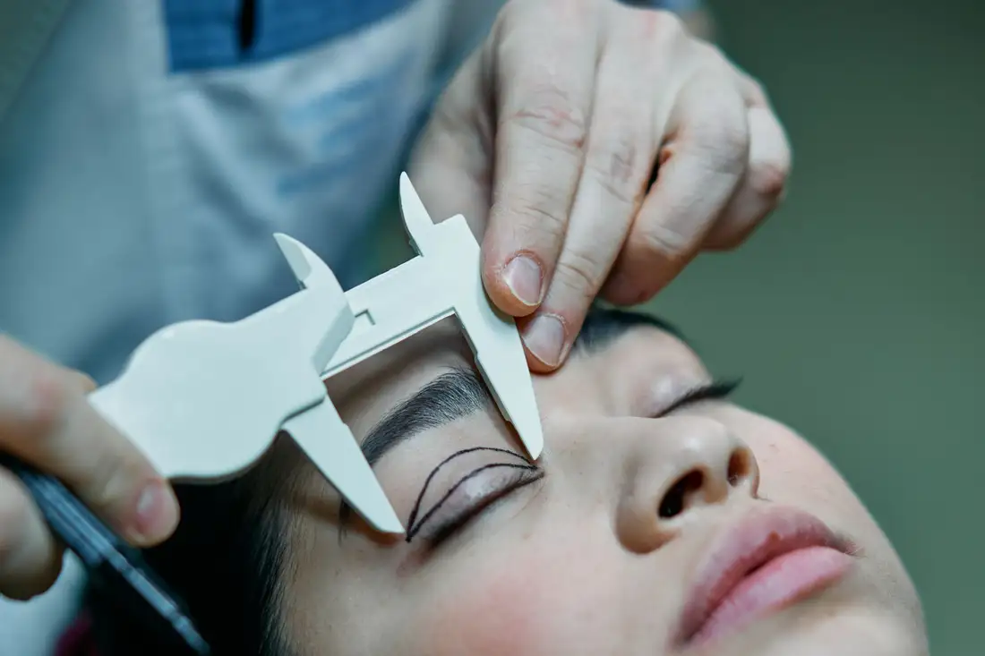 A surgeon's hands measuring a patient's eyelid with a caliper before marking it
