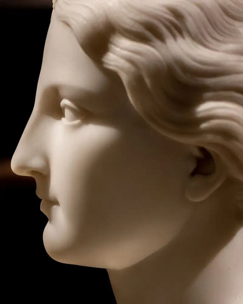 Profile of a marble sculpture's face against a dark gallery, the line of the nose lit from the side